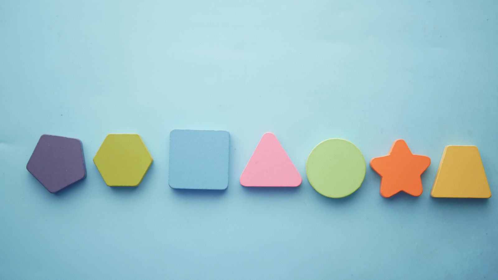 A row of colourful foam shapes, including a pentagon, hexagon, square, triangle, circle and star, on a light blue background
