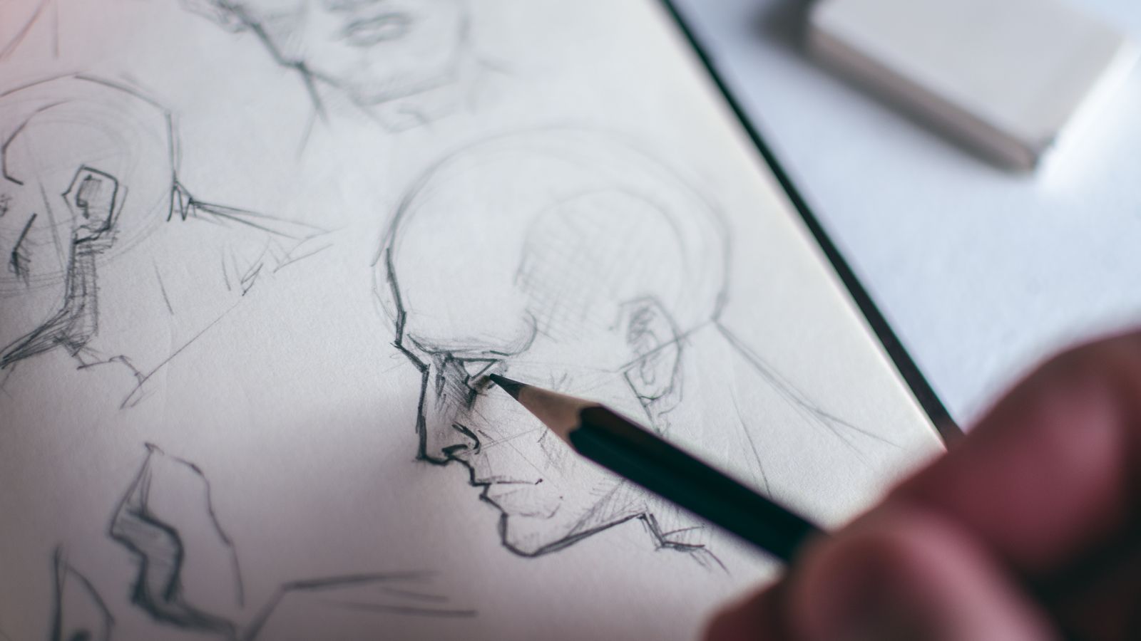 A hand holding a pencil, shading a sketch of a face in a notebook beside an eraser